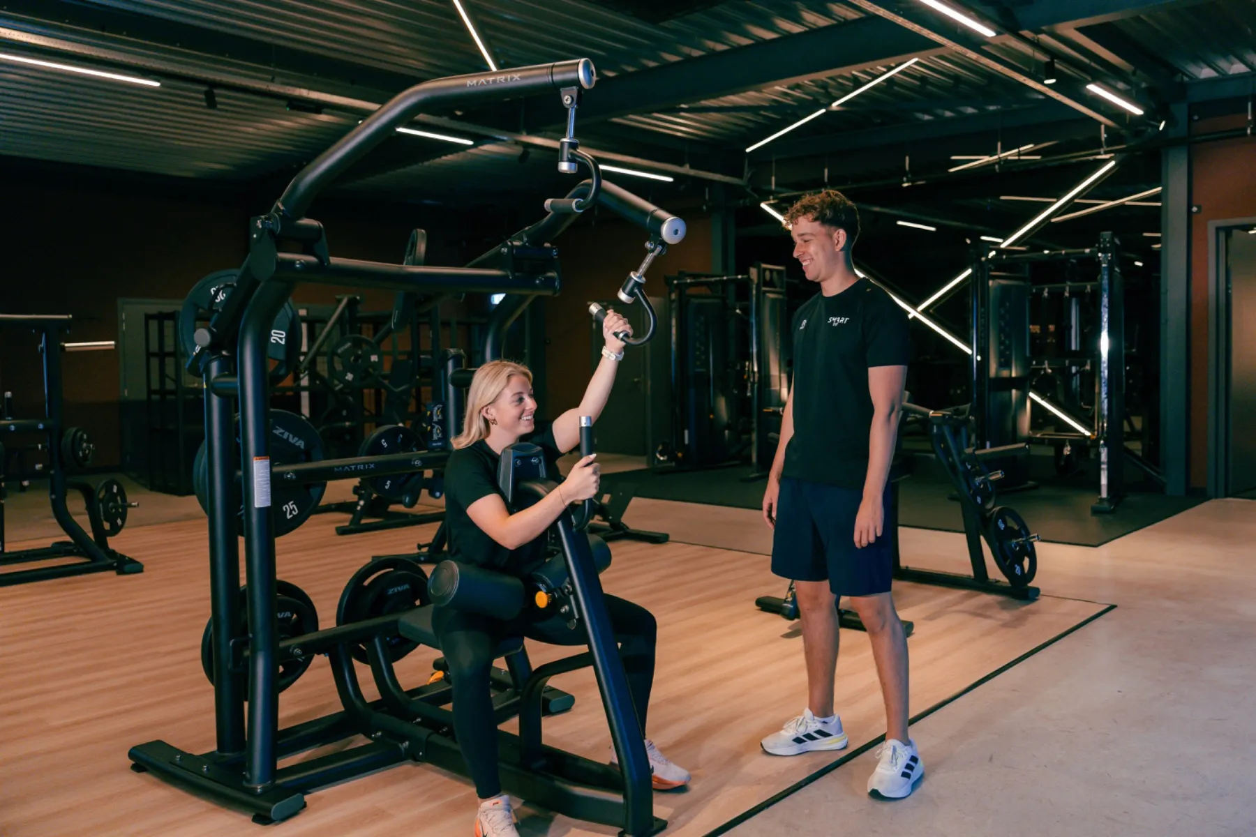 Trainer begeleidt een sporter op een krachtapparaat in de Smart Fit Sportstudio