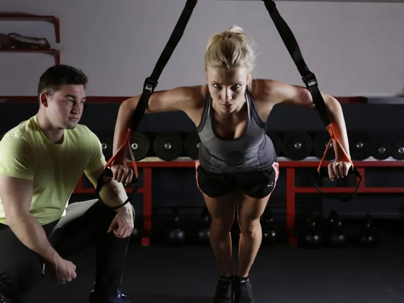 Trainer begeleidt een sporter bij een oefening met bandjes (voorbeeldfoto)